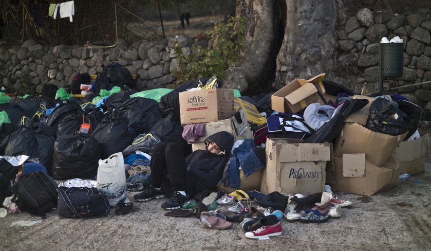 A Syrian refugee boy sleeps on a roadside amid donated clothes and shoes after he and his family arrived on a dinghy from the Turkish coast to the northeastern Greek island of Lesbos, Monday, Oct. 5 , 2015. (AP Photo/Muhammed Muheisen)