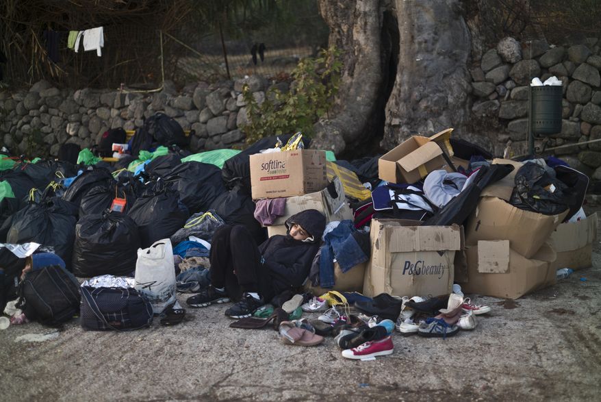 A Syrian refugee boy sleeps on a roadside amid donated clothes and shoes after he and his family arrived on a dinghy from the Turkish coast to the northeastern Greek island of Lesbos, Monday, Oct. 5 , 2015. (AP Photo/Muhammed Muheisen)