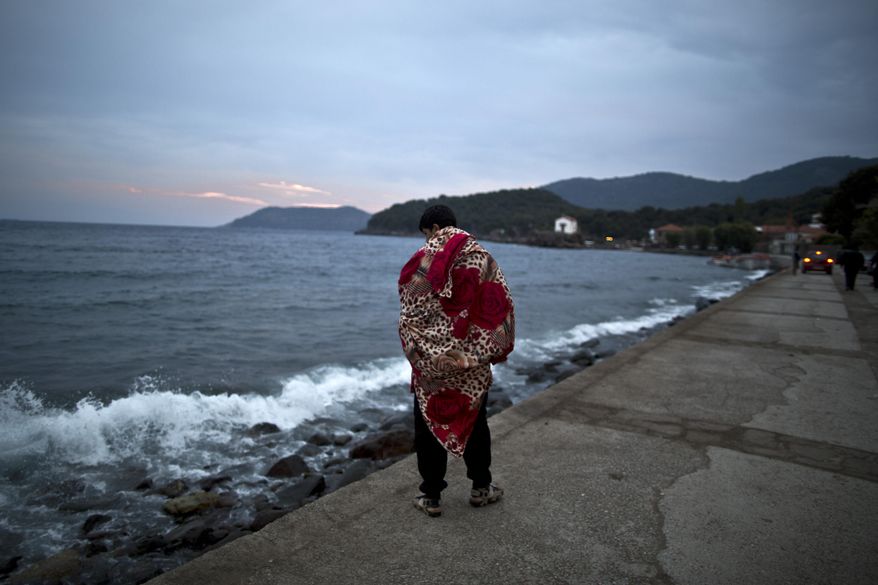 An Afghan refugee wrapped in a blanket walks by the sea after he and others arrived late in the night on a dinghy from the Turkish coast to the northeastern Greek island of Lesbos, early Thursday, Oct. 8 , 2015. More than 500,000 people have arrived in the European Union this year, seeking sanctuary or jobs and sparking the EU's biggest refugee emergency in decades. (AP Photo/Muhammed Muheisen)