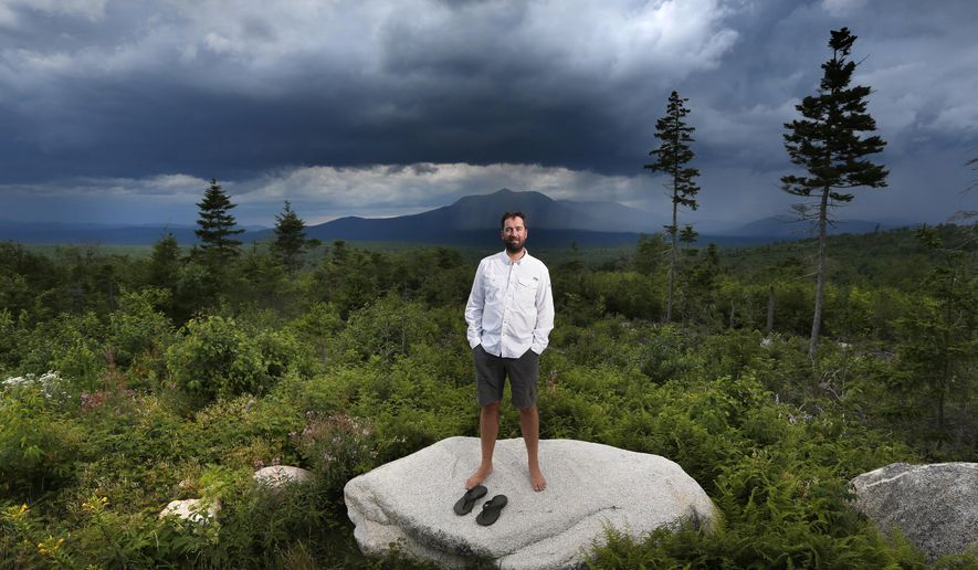 In this Tuesday, Aug. 4, 2015, photo, Lucas St. Clair poses on land proposed for a national park in Penobscot County, Maine. Mount Katahdin, the state's highest peak, can be seen in the background as a rainstorm passes through Baxter State Park. St. Clair is managing a non-profit foundation set up to promote the creation of a park on about 70,000 acres owned by his mother, Burt's Bees founder Roxanne Quimby. (AP Photo/Robert F. Bukaty)