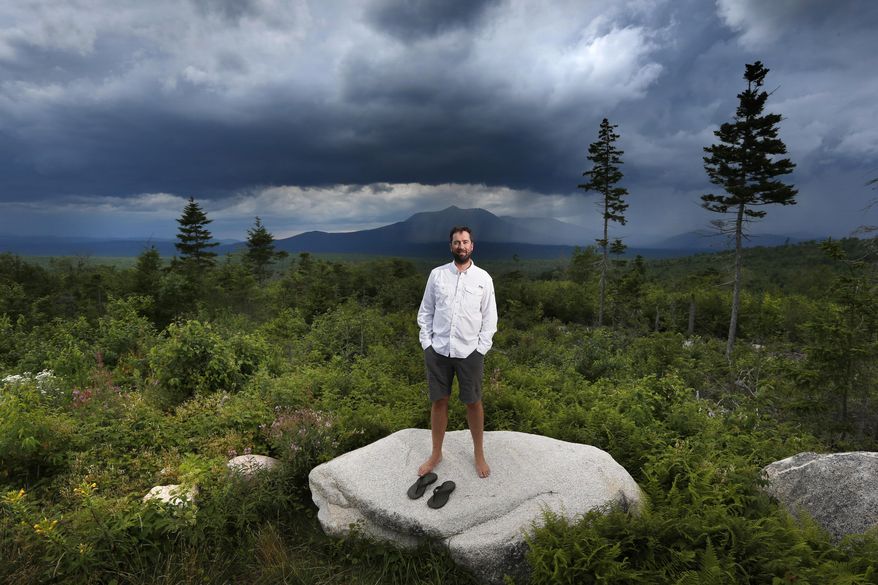 In this Tuesday, Aug. 4, 2015, photo, Lucas St. Clair poses on land proposed for a national park in Penobscot County, Maine. Mount Katahdin, the state's highest peak, can be seen in the background as a rainstorm passes through Baxter State Park. St. Clair is managing a non-profit foundation set up to promote the creation of a park on about 70,000 acres owned by his mother, Burt's Bees founder Roxanne Quimby. (AP Photo/Robert F. Bukaty)