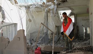 A Syrian soldier wrapped in a Syrian flag stands in a damaged house in Achan, Syria. Russian jets intensified their airstrikes Monday in the central Syrian province as government and allied troops pushed out insurgents from local villages to expand their control of the area, activists and a military statement said. (ASSOCIATED PRESS)