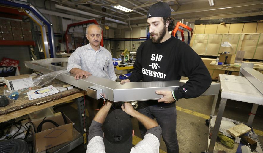 In a photo from Thursday, Oct. 8, 2015, in Warren, Mich., business owner Ismael Basha, left, looks on as Syrian refugee Mohammed Abo-Shaar, right, helps a co-worker assemble a frame. Basha, who came from Syria in the early 1980s, owns TSS Inc., which has 50 workers and makes automatic car wash fixtures and systems. Over the years, he said, he he’s hired refugees from Bosnia-Herzegovina, Serbia and Iraq, and, in recent weeks, several from Syria. He said they typically work hard and are dedicated. Many more are expected since the Obama administration pledged to accept about 10,000 Syrians in the next 12 months. (AP Photo/Carlos Osorio)