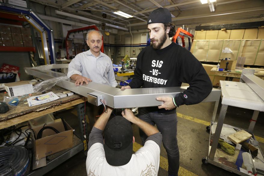In a photo from Thursday, Oct. 8, 2015, in Warren, Mich., business owner Ismael Basha, left, looks on as Syrian refugee Mohammed Abo-Shaar, right, helps a co-worker assemble a frame. Basha, who came from Syria in the early 1980s, owns TSS Inc., which has 50 workers and makes automatic car wash fixtures and systems. Over the years, he said, he he’s hired refugees from Bosnia-Herzegovina, Serbia and Iraq, and, in recent weeks, several from Syria. He said they typically work hard and are dedicated. Many more are expected since the Obama administration pledged to accept about 10,000 Syrians in the next 12 months. (AP Photo/Carlos Osorio)