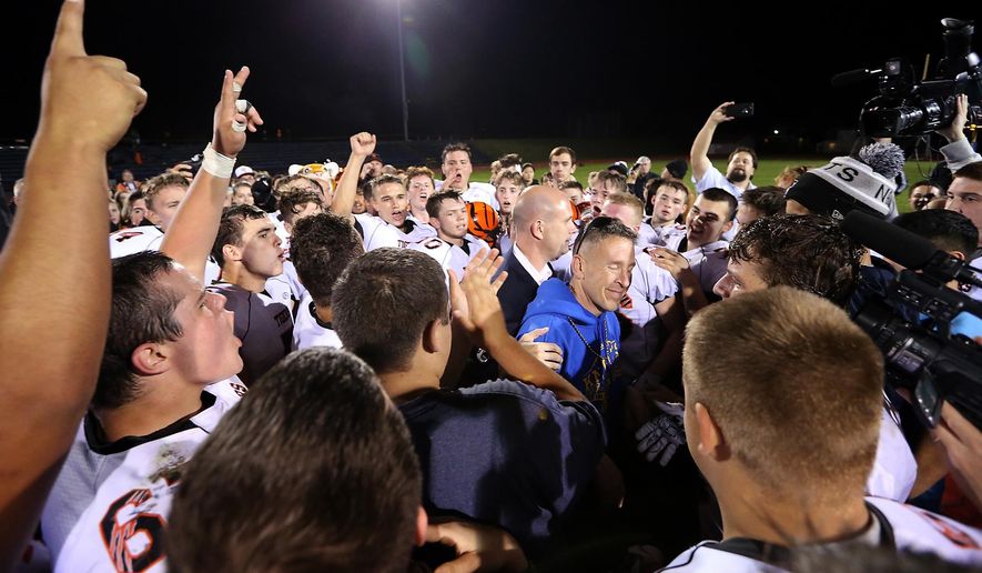 In this Friday, Oct. 16, 2015, photo, Bremerton assistant football coach Joe Kennedy, in blue, is surrounded by Centralia players after they took a knee with him and prayed after their game against Bremerton, in Bremerton, Wash. A Washington coach who was told by district officials to stop leading prayers after games went ahead with a prayer at the 50-yard line after a weekend game. (Meegan M. Reid/Kitsap Sun via AP) MANDATORY CREDIT