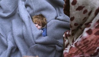 A migrant child is muffled up in blankets while resting on the road near a borderline between Serbia and Croatia, near the village of Berkasovo, Serbia, Tuesday, Oct. 20, 2015. (AP Photo/Darko Vojinovic)