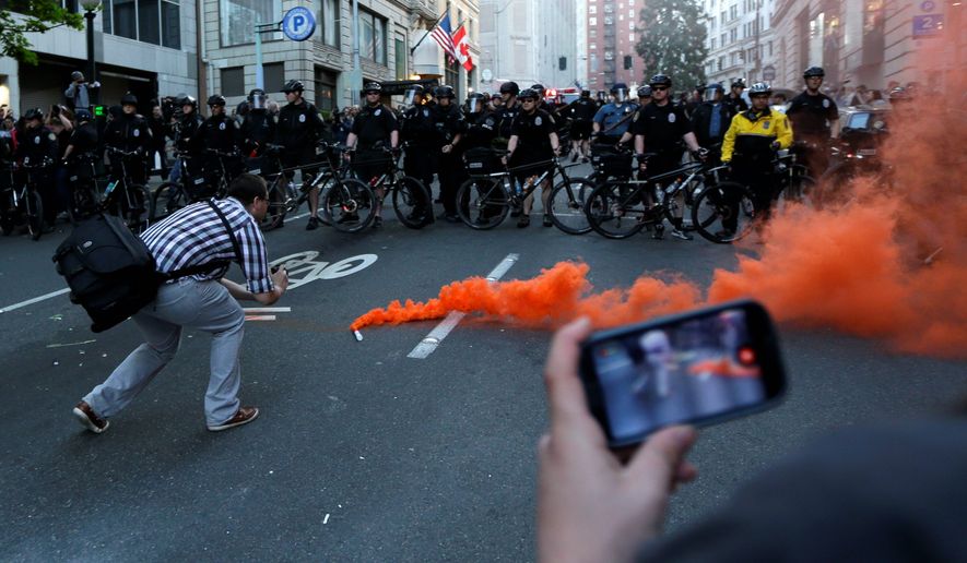 A man uses a mobile phone to record the scene after a smoke device was dropped in front of a row of Seattle Police officers during a May Day march that began as an anti-capitalism protest and turned into demonstrators clashing with police. Photos and video from the protest were widely shared on social media. (Associated Press)