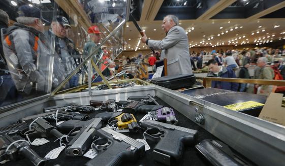 Handguns are displayed at the table of gun store owner David Petronis of Mechanicville, N.Y. as he holds a rifle during the annual New York State Arms Collectors Association Albany Gun Show in Albany, N.Y. (Associated Press) 