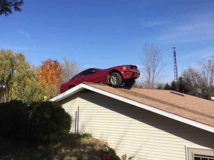 In this Oct. 26, 2015 photo provided by the Michigan State Police, a Ford Mustang is stopped on a roof of a house in Woodhull Township, Mich. State police say the driver had a medical problem and lost control of his car on Interstate 69 in Shiawassee County. (Michigan State Police via AP)