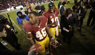 Washington Redskins quarterback Robert Griffin III,center, and teammate Alfred Morris wait to be interviewed after an NFL football game against the Dallas Cowboys on Sunday, Dec. 30, 2012, in Landover, Md. The Redskins won 28-18 to win the NFC East. (AP Photo/Evan Vucci)