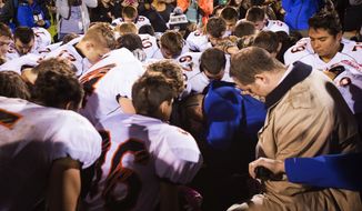 Bremerton (Wash.) High School assistant football coach Joe Kennedy (center) prays with his team despite orders to stop. Mr. Kennedy was subsequently placed on paid administrative leave. (Seattle Times via Associated Press)