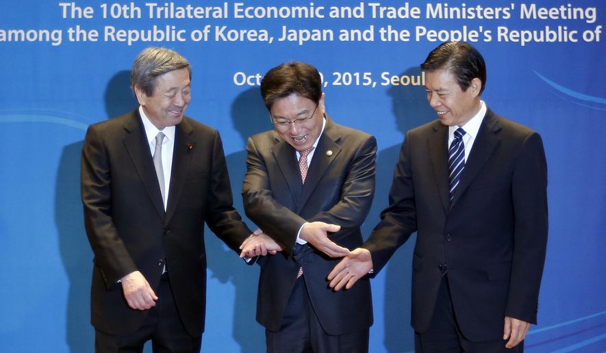 South Korea's Trade, Industry and Energy Minister Yoon Sang-jick, center, tries to hold hands to pose for the media with Japan's Economy, Trade and Industry Minister Motoo Hayashi, left, and China International Trade Representative Zhong Shan before the 10th trilateral economic and trade ministers' meeting in Seoul, South Korea, Friday, Oct. 30, 2015. Three Asian countries will discuss about their economic cooperation and the FTA or Free Trade Agreement. (AP Photo/Lee Jin-man)