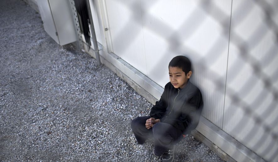 A boy sits inside an enclosure at the migrant and refugee registration camp in Moria, on the island of Lesbos, Greece, Thursday, Nov. 5, 2015. The European Union predict that around 3 million more migrants are expected to arrive in the 28-nation bloc by the end of next year. (AP Photo/Marko Drobnjakovic)