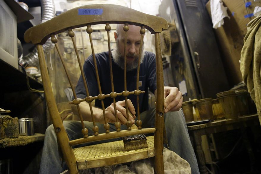 In this Thursday, Nov. 5, 2015, photo, Sean Bausert stains a chair at the Veterans Caning & Repair shop in New York. In a dusty, cluttered shop that seems oddly out of place in modern New York, a group of artisans is among the last still practicing a dying trade: chair caning. The painstaking art of weaving furniture details in a honeycomb pattern is still in demand, mostly for repair work, but the shop that's been around since the 1860s is under threat from a new wave of high-rise development on Manhattan's west side. (AP Photo/Mary Altaffer)