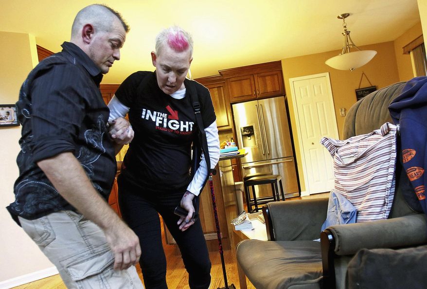 In this Oct. 22, 2015 photo, Meghan Korbecki, who is battling brain cancer for the third time, has help getting into a chair from husband, Bill, before dinner at their home in Crystal Lake, Ill. (Matthew Apgar/Northwest Herald via AP) CHICAGO TRIBUNE OUT, MANDATORY CREDIT