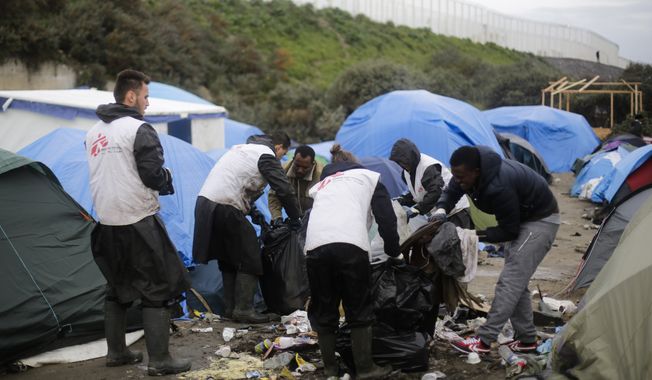 Migrants help a Doctors Without Borders collection crew to take way garbage at the migrants camp near Calais, northern France, in this Nov. 6, 2015, file photo. Residents of France’s biggest refugee camp near the English Channel port of Calais must combat hunger, filth and illness in a tent village as they scramble to build hard roofs for the winter. (AP Photo/Markus Schreiber)