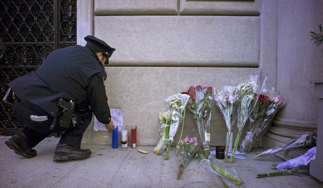 A New York City police officer adjusts parts of a make shift memorial left as a sign of support to France near the door of the French consulate in New York, Saturday, Nov. 14, 2015. French officials say several dozen people were killed in shootings and explosions at a theater, restaurant and elsewhere in Paris on Friday. (AP Photo/Craig Ruttle)