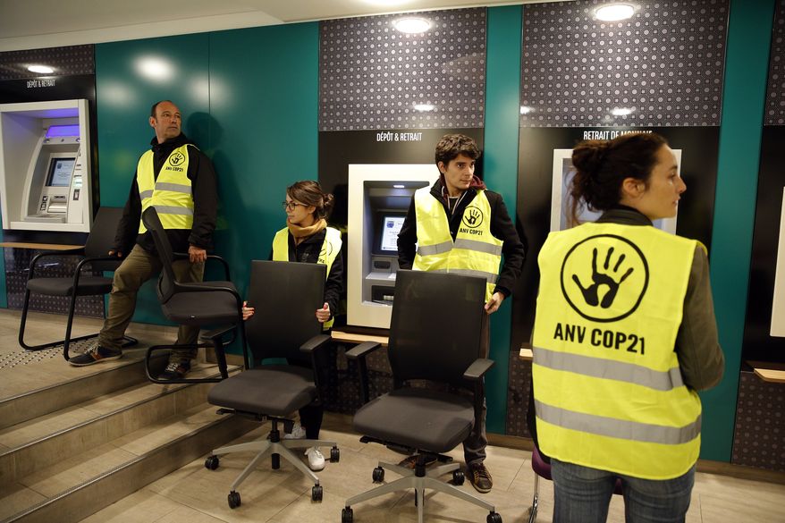 Activists in Paris take chairs from a bank to protest tax evasion, one of many actions linked to the climate conference known as COP21. A march and other activities have been canceled, however, as a result of terrorist attacks in the city last week. (Associated Press)