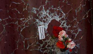 Flowers are put in a window shattered by a bullet as a forensic marker sits next to the impact as people pay their respect to the victims at the site of the attacks on restaurant Le Petit Cambodge (Little Cambodia) and the Carillon Hotel on the first of three days of national mourning in Paris, Sunday, Nov. 15, 2015. Thousands of French troops deployed around Paris on Sunday and tourist sites stood shuttered in one of the most visited cities on Earth while investigators questioned the relatives of a suspected suicide bomber involved in the country&#39;s deadliest violence since World War II. (AP Photo/Peter Dejong)
