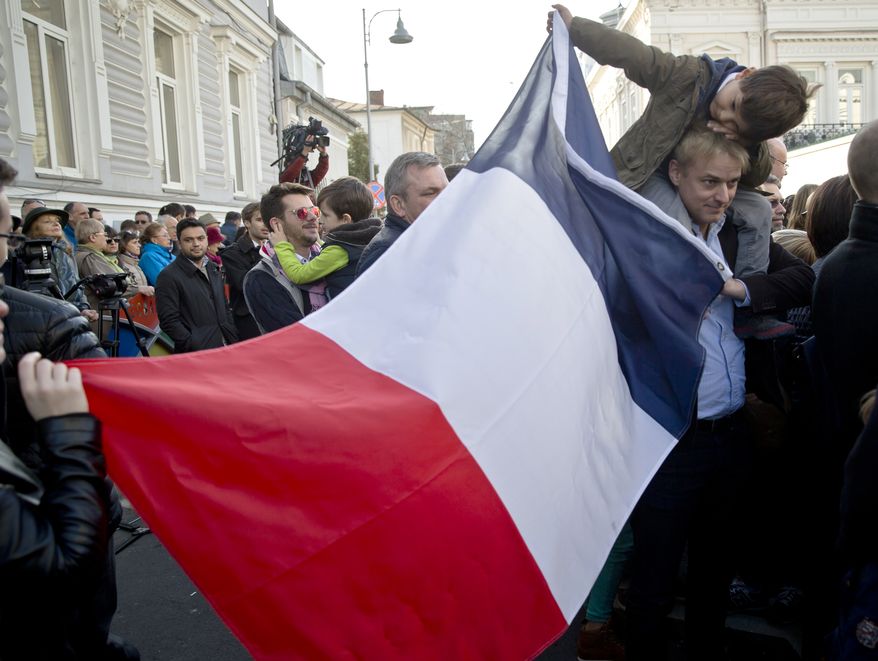 People hold a French flag while waiting to pay respects to victims of the terrorist attacks at the French Embassy in Bucharest, Romania, Sunday, Nov. 15, 2015. Multiple terrorist attacks across Paris on Friday night have left more than one hundred dead and many more injured. (AP Photo/Vadim Ghirda)