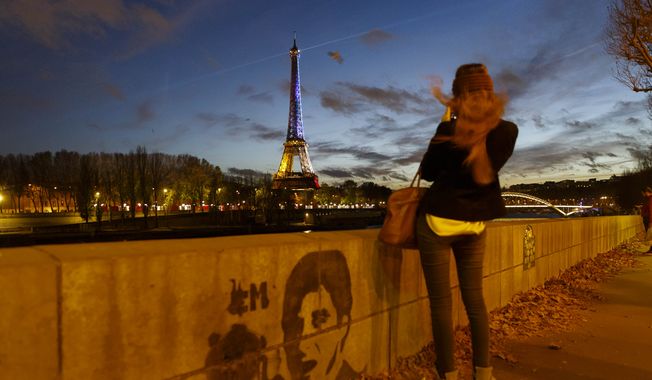 A girl takes a picture from the banks of the River Seine of the illuminated Eiffel Tower in the French national colors red, white and blue in honor of the victims of the terrorist attacks last Friday, in Paris, Wednesday, Nov. 18, 2015. (AP Photo/Daniel Ochoa de Olza)

