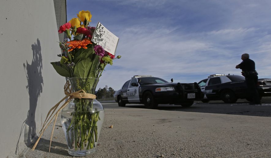 Flowers are left by the side of the road as a San Bernardino police officer blocks the road leading to the site of yesterday&#39;s mass shooting on Thursday, Dec. 3, 2015 in San Bernardino, Calif.  A heavily armed man and woman dressed for battle opened fire on a holiday banquet for his co-workers Wednesday, killing multiple people and seriously wounding others in a precision assault, authorities said. Hours later, they died in a shootout with police. (AP Photo/Chris Carlson)