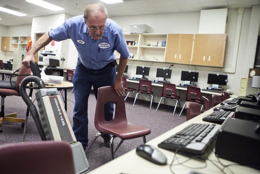 In this Dec. 4, 2015 photo, Bob Stevens vacuums under the tables in the computer room at Corral Drive Elementary in Rapid City, S.D. Stevens is among support-services workers seeking higher pay from the Rapid City Area Schools. Wage negotiations between Rapid City School District officials and support-services employees have disintegrated. The local Teamsters union recently announced that due to a lack of supportive membership, it would no longer represent the employees at the negotiating table. They include custodians, maintenance staff, bus drivers, warehouse workers, grounds workers, security personnel, mechanics, laundry staff and print shop workers. (Sean Ryan/Rapid City Journal via AP)  TV OUT; MANDATORY CREDIT