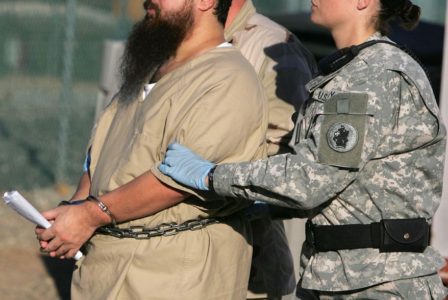 FILE - In this Dec. 6, 2006 file photo, reviewed by a U.S. Dept of Defense official, a shackled detainee is transported by a female guard, front, and male guard, behind, away from his annual Administrative Review Board hearing with U.S. officials, at Camp Delta detention center, Guantanamo Bay U.S. Naval Base, Cuba. A U.S. Army officer told a court on Tuesday, Dec. 8, 2015 that she started to use women to transport prisoners in 2014 due to a shortage of guards. A judge has issued a temporary ban the military is seeking to lift. Muslim prisoners say contact with unrelated females violates their religion. (AP Photo/Brennan Linsley, File)