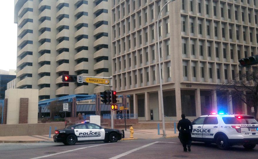 Police gather outside of Albuquerque City Hall, Friday, Dec. 11, 2015. Authorities say City Hall has been placed on lockdown after witnesses say they saw a person with gun inside. Police said authorities don't believe an active shooter was in the area, which includes Downtown Albuquerque. However, a person was seen inside the building armed with a gun and causing a disturbance. (AP Photo/Mary Hudetz)