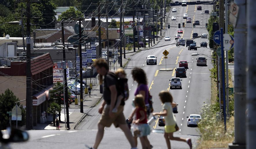 FILE - In this Tuesday, July 14, 2015, file photo, pedestrians cross the wide swath of 82nd Avenue in East Portland, Ore. The Avenue is traditionally considered the dividing line between Portland and East Portland, where shabby apartment complexes, fading strip malls, wide avenues and fast-food chains are the norm. Community leaders say Portland must do more to stop the displacement of residents caused by gentrification. Low-income and immigrant families say they're being pushed out of East Portland, a historically neglected part of town. Portland's tight rental market, coupled with new public and private investments in East Portland, are making the area more desirable to middle class residents. (AP Photo/Don Ryan, File)
