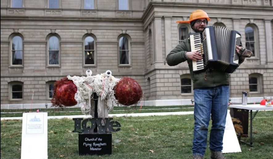 A Pastafarian stands next to a display of the Flying Spaghetti Monster erected alongside nativity and hanukkah displays outside the Michigan state capitol. (Image: Twitter @danielleaduval)