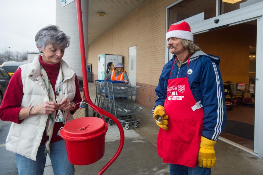 In this photo taken on Monday, Dec. 21, 2015, Deb Dingman drops money into a red kettle as David Pringle ring his bell for the Salvation Army Red Kettle Drive in front of a Kroger supermarket, in Hampton Township, Mich. (Yfat Yossifor/The Bay City Times via AP) LOCAL TELEVISION OUT; LOCAL INTERNET OUT; MANDATORY CREDIT