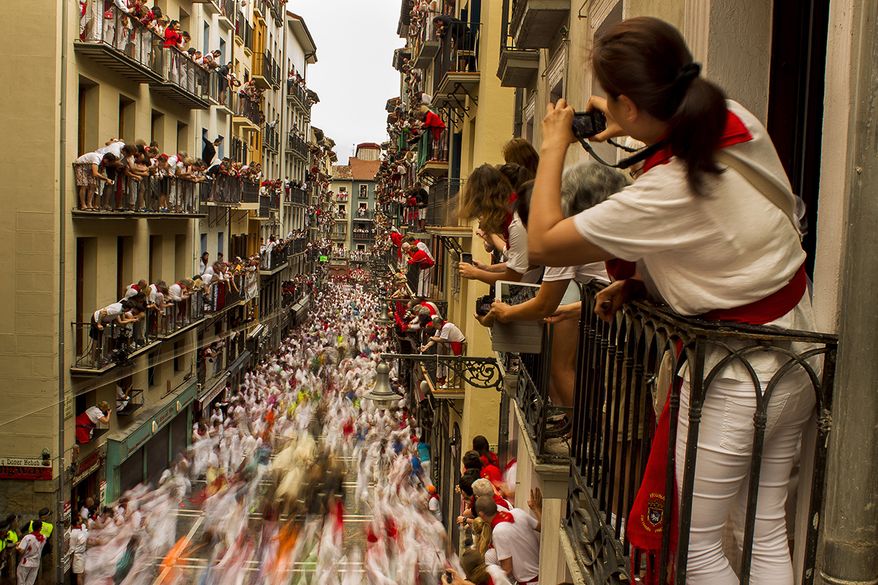 People watch as El Tajo y La Reina fighting bulls and revelers run during the running of the bulls, at the San Fermin festival, in Pamplona, Spain, Wednesday, July 8, 2015. Revelers from around the world arrive to Pamplona every year to take part in some of the eight days of the running of the bulls. (AP Photo/Andres Kudacki, File)