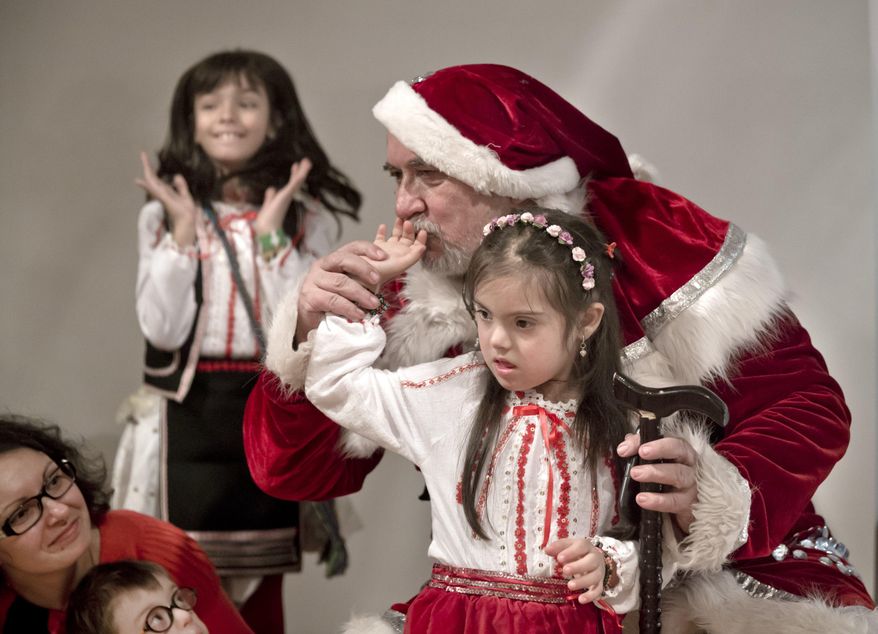 In this Friday, Dec. 18, 2015 image a man dressed as Santa Claus kisses the hand of a girl as another one reacts with joy during a Christmas party for children affected by the Down Syndrome, organized by the Angels Down Friends association in Bucharest, Romania. Angels Down Friends, founded in 2013 by the parents of a child with Down syndrome, organized the event to encourage parents of children with the condition and with the long-term goal of more fully integrating youngsters with Down into society. (AP Photo/Vadim Ghirda)