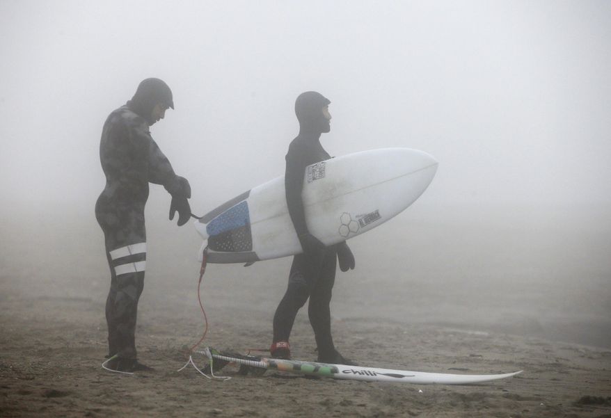 Enveloped by dense fog, two surfers prepare to enter the Atlantic Ocean from Rockaway Beach on Christmas Day, Friday, Dec. 25, 2015, in New York. With temperatures well above normal for this time of year, and tides higher than they've been in a while, surfers said conditions were ideal and they planned to take advantage of the unusually warm weather. (AP Photo/Kathy Willens)