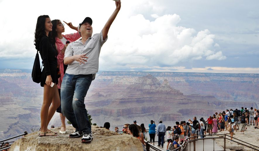In this Aug. 2, 2015, photo, tourists Joseph Lin, Ning Chao, center, and Linda Wang, left, pose for a selfie along the south rim at Grand Canyon National Park, Ariz. The throngs of tourists have been showing up in big numbers at other national parks, including Yellowstone in Wyoming, Yosemite in California and Zion in Utah, driven by good weather, cheap gas and marketing campaigns ahead of next year's National Park Service centennial. (Emery Cowan/Arizona Daily Sun via AP/File) MANDATORY CREDIT