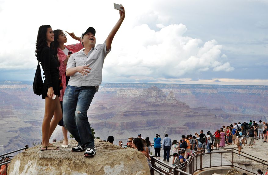 In this Aug. 2, 2015, photo, tourists Joseph Lin, Ning Chao, center, and Linda Wang, left, pose for a selfie along the south rim at Grand Canyon National Park, Ariz. The throngs of tourists have been showing up in big numbers at other national parks, including Yellowstone in Wyoming, Yosemite in California and Zion in Utah, driven by good weather, cheap gas and marketing campaigns ahead of next year's National Park Service centennial. (Emery Cowan/Arizona Daily Sun via AP/File) MANDATORY CREDIT