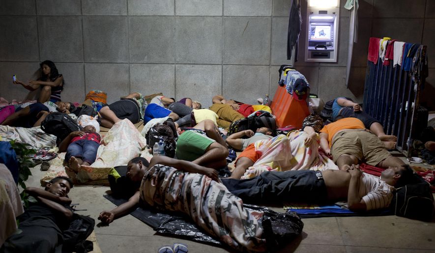 FILE - In this Nov. 21, 2015 file photo, a Cuban woman migrant uses her cell phone while other Cubans sleep, outside of the border control building in Penas Blancas, Costa Rica, on the border with Nicaragua which closed its borders to Cuban migrants. The Costa Rican Foreign Ministry said in a Dec. 28 statement that the first humanitarian transfer will airlift the Cuban migrants from that country to El Salvador in January. From there they will continue by bus toward Mexico. The number of Cubans stranded in Costa Rica has reached at least 8,000 since neighboring Nicaragua closed its border to them weeks ago. (AP Photo/Esteban Felix, File)