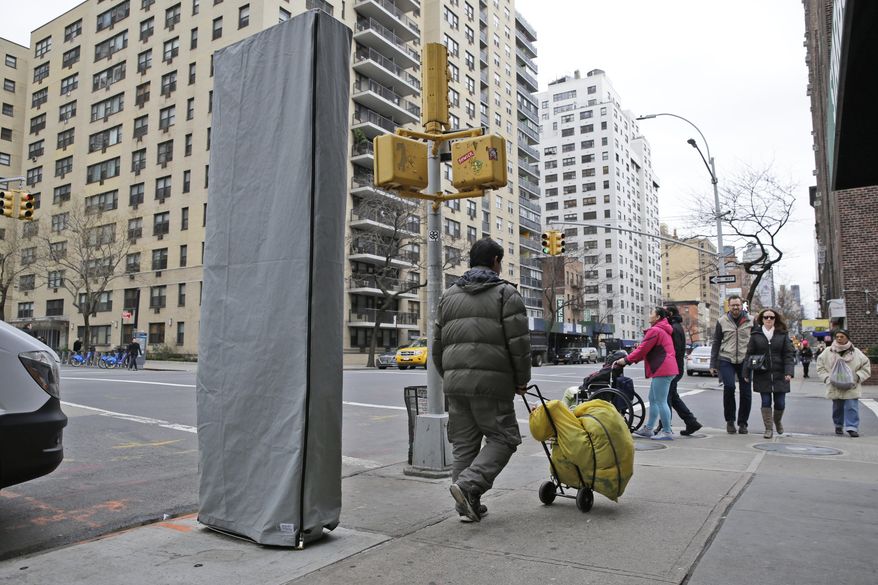 In this photo taken on Thursday, Dec. 31, 2015, people walk near a covered wireless kiosk at an intersection in New York. The 9-foot-tall, narrow structure installed this past week on a Manhattan sidewalk is signaling a plan to turn payphones into what's billed as the world's biggest and fastest municipal Wi-Fi network. The first of at least 7,500 planned hot spots are due to go online early next year, promising superfast and free Wi-Fi service, new street phones with free calling, ports to charge personal phones and a no-cost windfall for the city. (AP Photo/Seth Wenig)