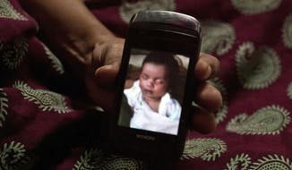 In this Nov. 4, 2015, photo, Amita Parmar, 30, displays a photograph of a South African child she was a surrogate for, in Anand, India. The Indian government recently banned surrogate services for foreigners and ordered fertility clinics to stop the practice of hiring Indian women to bear children for them. (AP Photo/Allison Joyce) ** FILE **