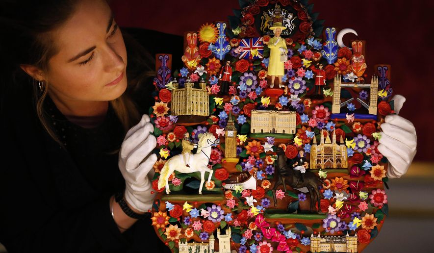 FILE- In this July 23, 2015 file photo, an employee of the Royal Collection Trust looks at the Tree of Life, a gift presented to Britain's Queen Elizabeth II from Mexican President Enrique Pena Nieto in 2015, during a press preview for the Summer opening of Buckingham Palace in London, A list of official gifts received by Queen Elizabeth II from world leaders and dignitaries during 2015 features jewelry, ornaments and some more unusual choices — including homemade honey butter from Michelle Obama. (AP Photo/Frank Augstein, File)