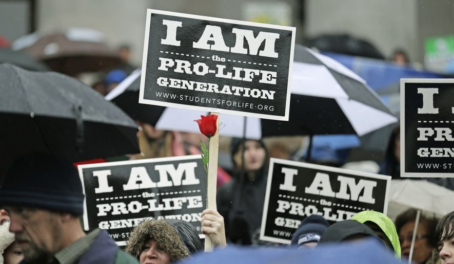 A pro-life demonstrator holds a sign and a flower while cheering during a rally, Tuesday, Jan. 19, 2016, at the Capitol in Olympia, Wash. (AP Photo/Ted S. Warren) ** FILE **