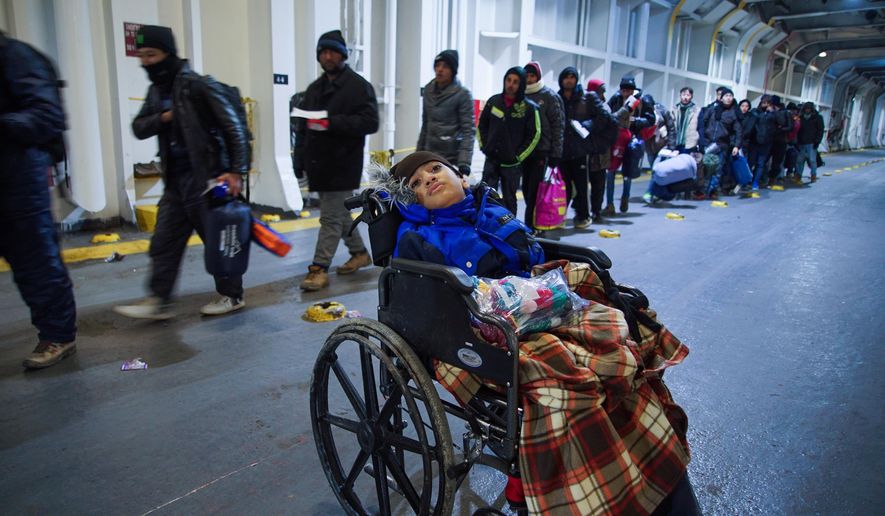 A child in a wheelchair waits as migrants queue up to have their tickets checked as they board the ferry to Athens, on Lesbos Island, Greece, Sunday, Jan. 24, 2016. (AP Photo/Mstyslav Chernov)