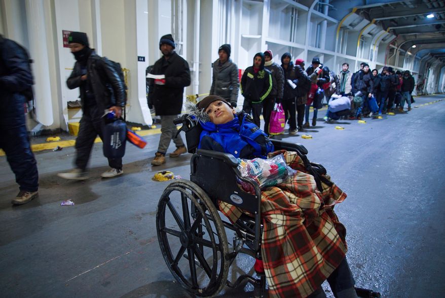 A child in a wheelchair waits as migrants queue up to have their tickets checked as they board the ferry to Athens, on Lesbos Island, Greece, Sunday, Jan. 24, 2016. (AP Photo/Mstyslav Chernov)
