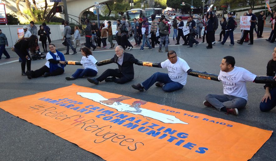 Immigration activists tied together by the arms participate in a sit-in protest against the raids and deportation of immigrants, on Tuesday, Jan. 26, 2016 near the downtown Los Angeles Federal Building. Organizers said in a news release they would be demanding a stop to deportation of Central American immigrant families and recognition that they are refugees seeking asylum. (AP Photo/Edwin Tamara)