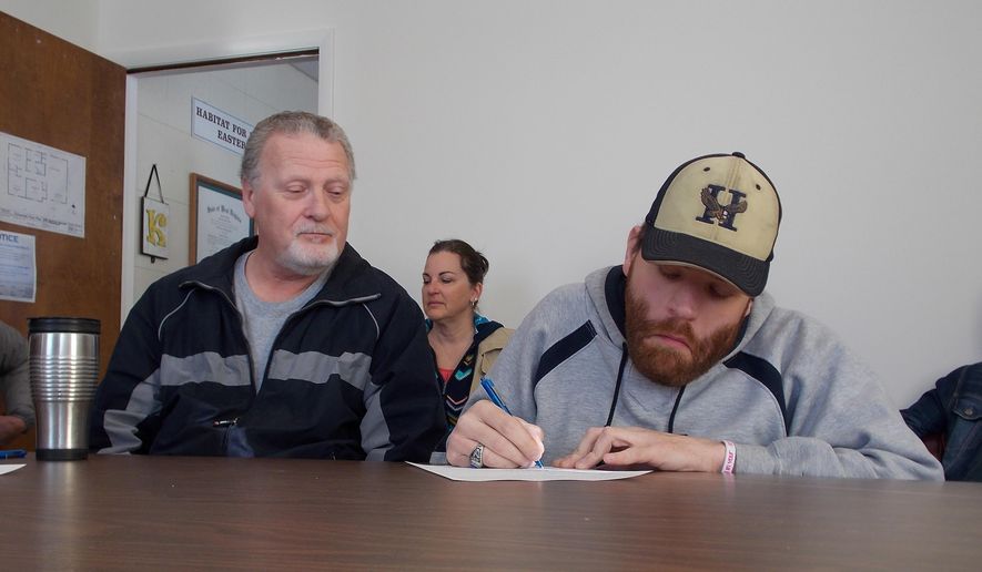 ADVANCE FOR MONDAY FEB. 8 AND THEREAFTER This Monday Feb. 1, 2016 photo shows Shane Unger, right, as he signs papers Tuesday for a new Habitat for Humanity of the Eastern Panhandle home, while his father , Mike, looks on in Martinsburg, W.Va. (John McVey/The Journal via AP)
