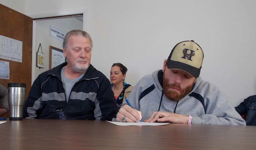 ADVANCE FOR MONDAY FEB. 8 AND THEREAFTER This Monday Feb. 1, 2016 photo shows Shane Unger, right, as he signs papers Tuesday for a new Habitat for Humanity of the Eastern Panhandle home, while his father , Mike, looks on in Martinsburg, W.Va. (John McVey/The Journal via AP)