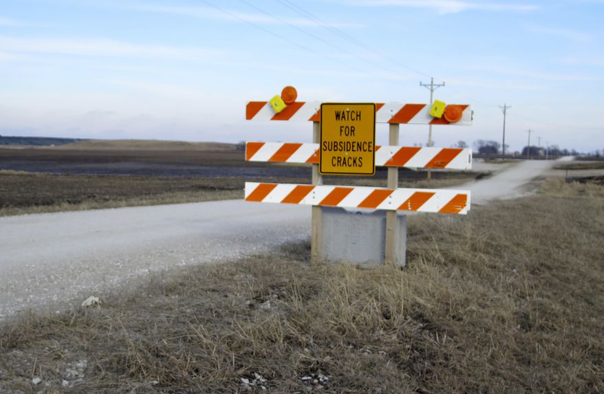 In this Feb. 5, 2016 photo, a traffic sign near the Deer Run coal mine near Hillsboro in southern Illinois warns motorists to be aware of cracks in the road caused by settling of the ground from mining, a process known as subsidence. Mine owner Peabody Energy is asking state regulators to approve a 7,731-acre expansion that is opposed by some residents who fear it could jeopardize public health and cause environmental damage. A smoldering underground fire has led the company to idle its operations (AP Photo/Alan Scher Zagier)