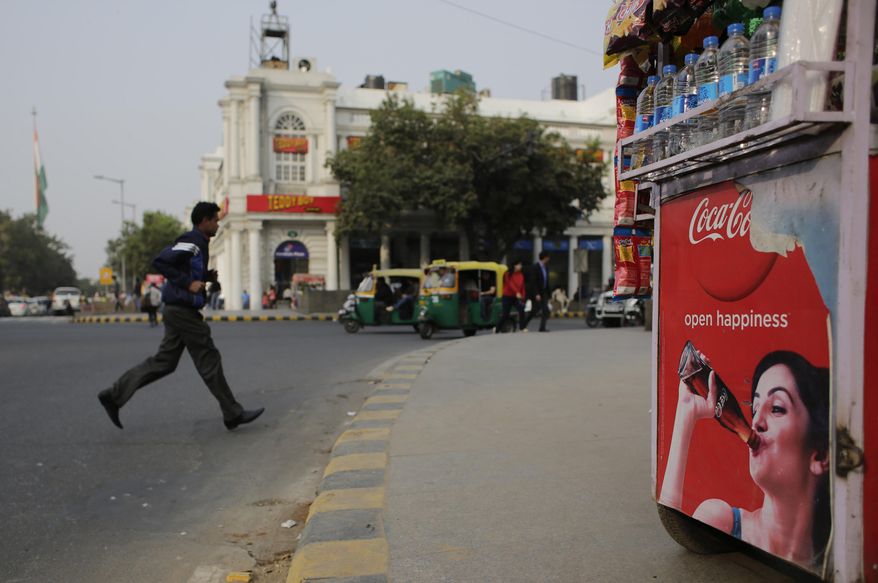 An Indian pedestrian crosses a road near roadside kiosk with a Coca-cola advertisement in New Delhi, India, Friday, Feb. 12, 2016. Coca-Cola suspended bottling at three plants in India, including one in the parched northwest where farmers have been protesting the company's use of dwindling groundwater reserves. (AP Photo/Altaf Qadri)