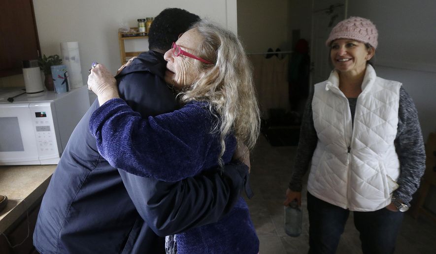 In this Tuesday, Jan. 19, 2016 photo, Lorindra Frances, a spiritual healer who lived at Harbin Hot Springs before it closed after September 2015 wildfires, center, hugs Federal Emergency Management Agency (FEMA) spokesman Victor Inge as Dena Barron, co-owner of Lake Village Estates, watches in Frances's housing unit in Clearlake Oaks, Calif. Five months after a Northern California wildfire killed four and wiped out homes, many Lake County residents face personal and logistical hurdles that put full recovery years away, if ever, for some. (AP Photo/Jeff Chiu)